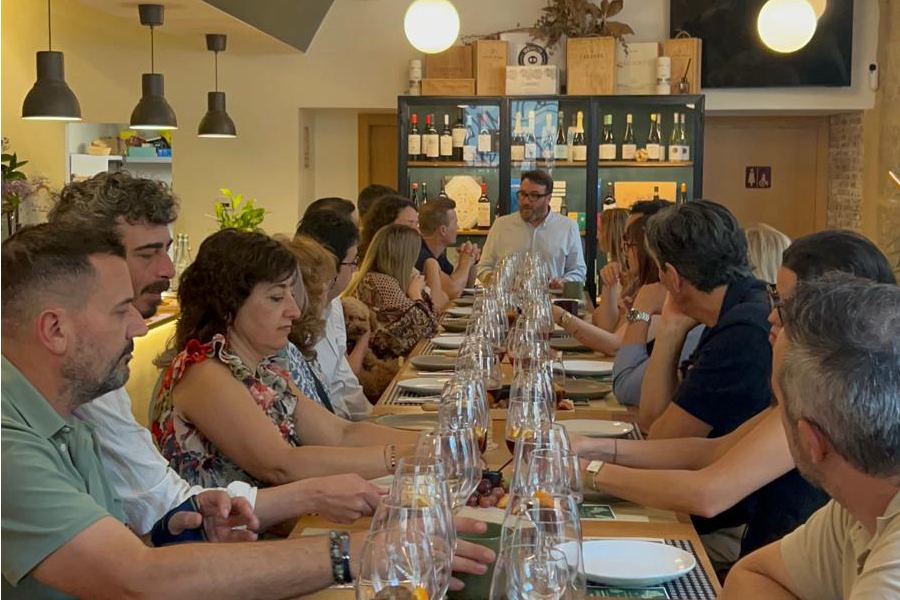 Cata privada en mesa larga con copas de vino y estanterías de botellas al fondo